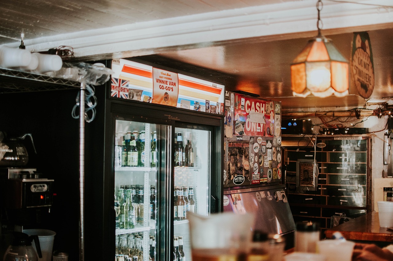 Bar interior with commercial drinks fridge stocked with beer bottles and signage inside a licensed hospitality venue.