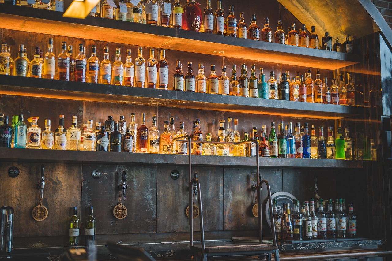 Backlit bar shelves lined with premium spirits and wine bottles in a modern licensed venue with beer taps below.