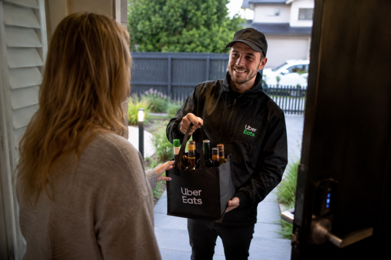 Alcohol delivery driver handing a bag containing alcoholic beverages to a customer at the front door of a private home.